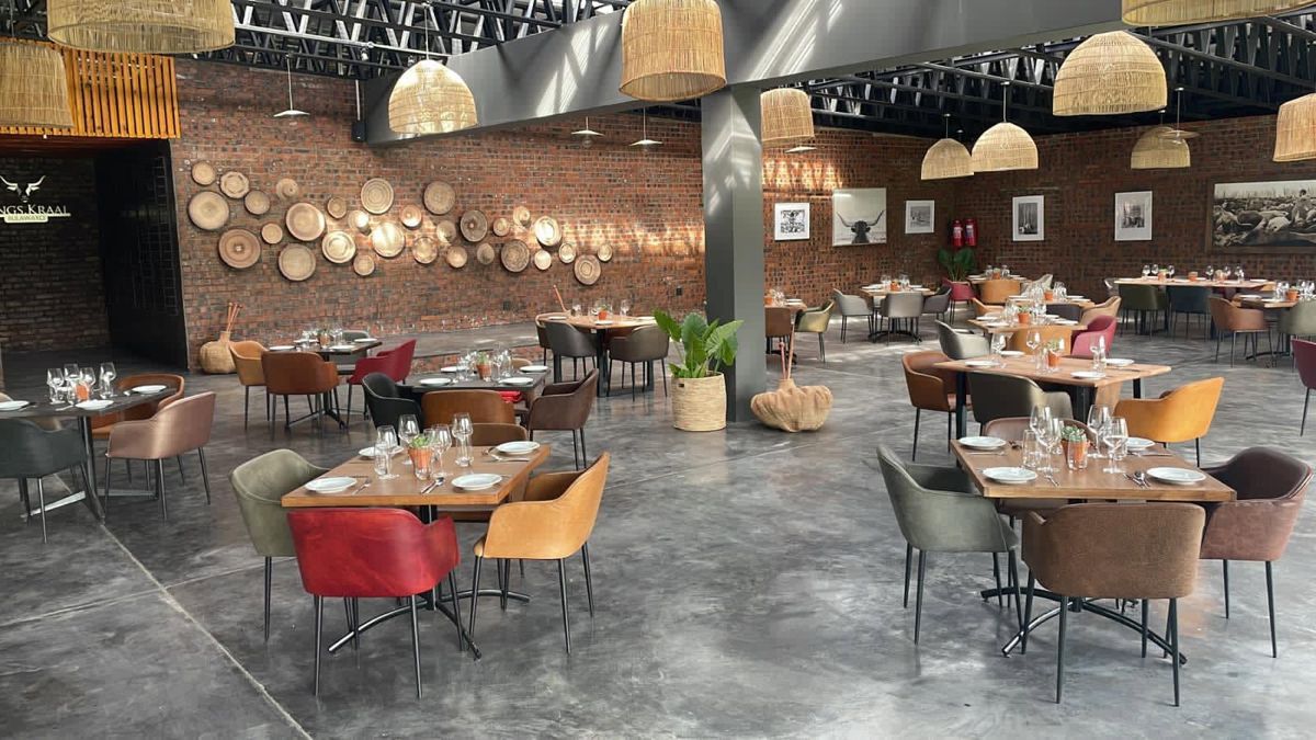 Kings Kraal dining room: exposed brick walls hung with woven baskets, rattan pendant lights and wooden tables with leather chairs in mixed colours